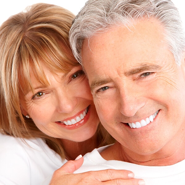 A mature woman and her husband hugging and smiling with their dentures
