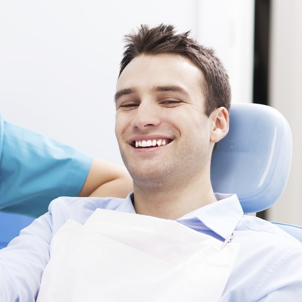 Young man sitting in a blue dental treatment chair laughing with his restorative dentist