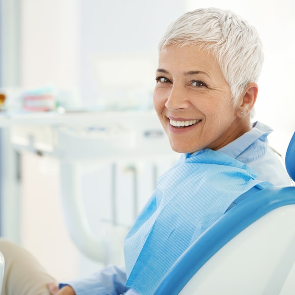 Mature woman with grey hair and blue top looking back and smiling because of her new dental crowns