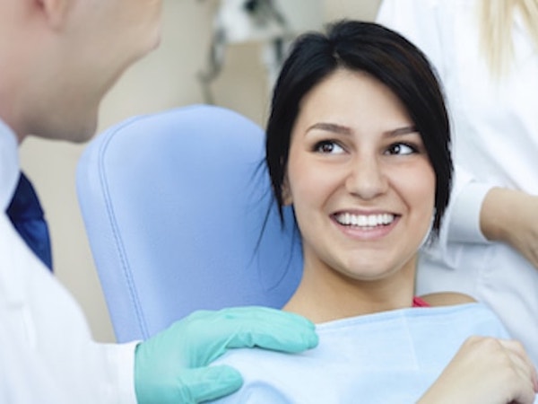 A dentist explaining different services to a woman with dark hair sitting in dental chair