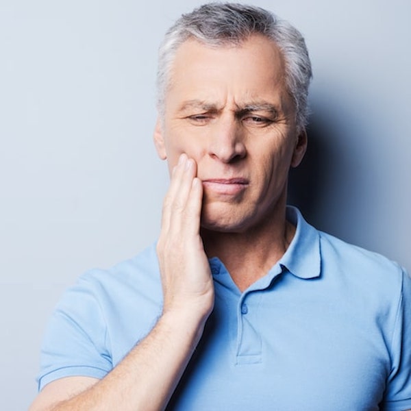 A man in a light blue top holding the side of his face in pain